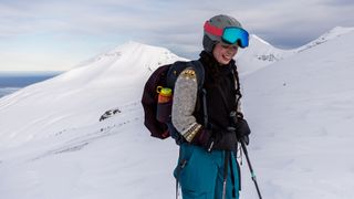 A woman wearing ski gear and SunGod Ullrs goggles stands on a snowy mountainside, smiling