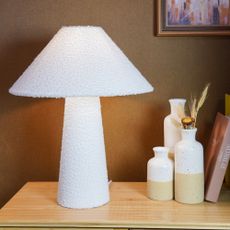 The Range Cream Boucle Effect Table Lamp set against a brown wall on a sideboard with bud vases next to it