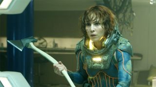 A still from the movie Prometheus. Here we see a dishevelled woman with chin-length light brown hair and dark eyes wearing a spacesuit. She is holding up an axe, ready to fight.