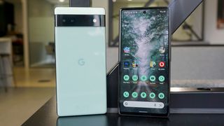 The Google Pixel 6a from the front and back, stood on a table