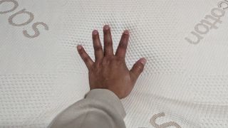 A hand pressing down on the Saatva Graphite Memory Foam Mattress Topper