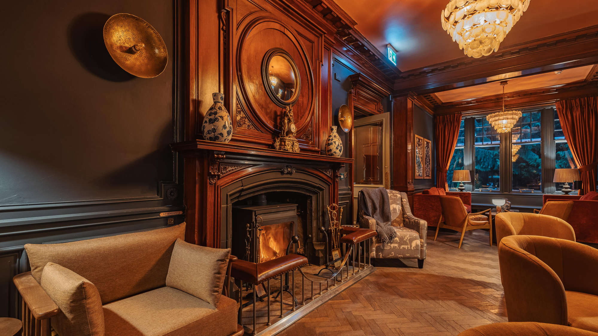 The reception and lounge area of the Pine Trees hotel, with panelled walls, armchairs and a real fire