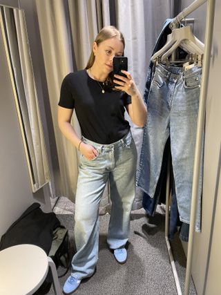 Woman in dressing room wears black t-shirt, blue jeans, blue trainers
