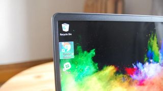Close-up of a laptop screen showing colorful abstract wallpaper with Recycle Bin, Google Chrome, and Slack icons in the top left corner. Warm, inviting setting.