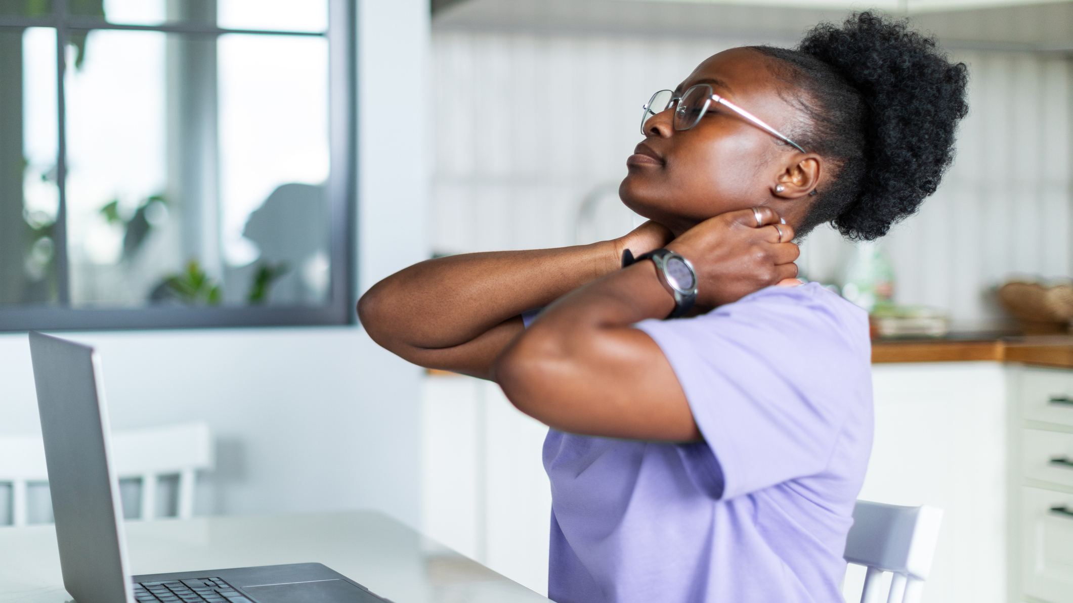 Woman sitting at a desk in front of a laptop holds her neck in both hands