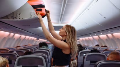 Woman putting a suitcase in the overhead bin on a plane