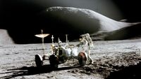 An astronaut standing next to a car-like vehicle on the moon.