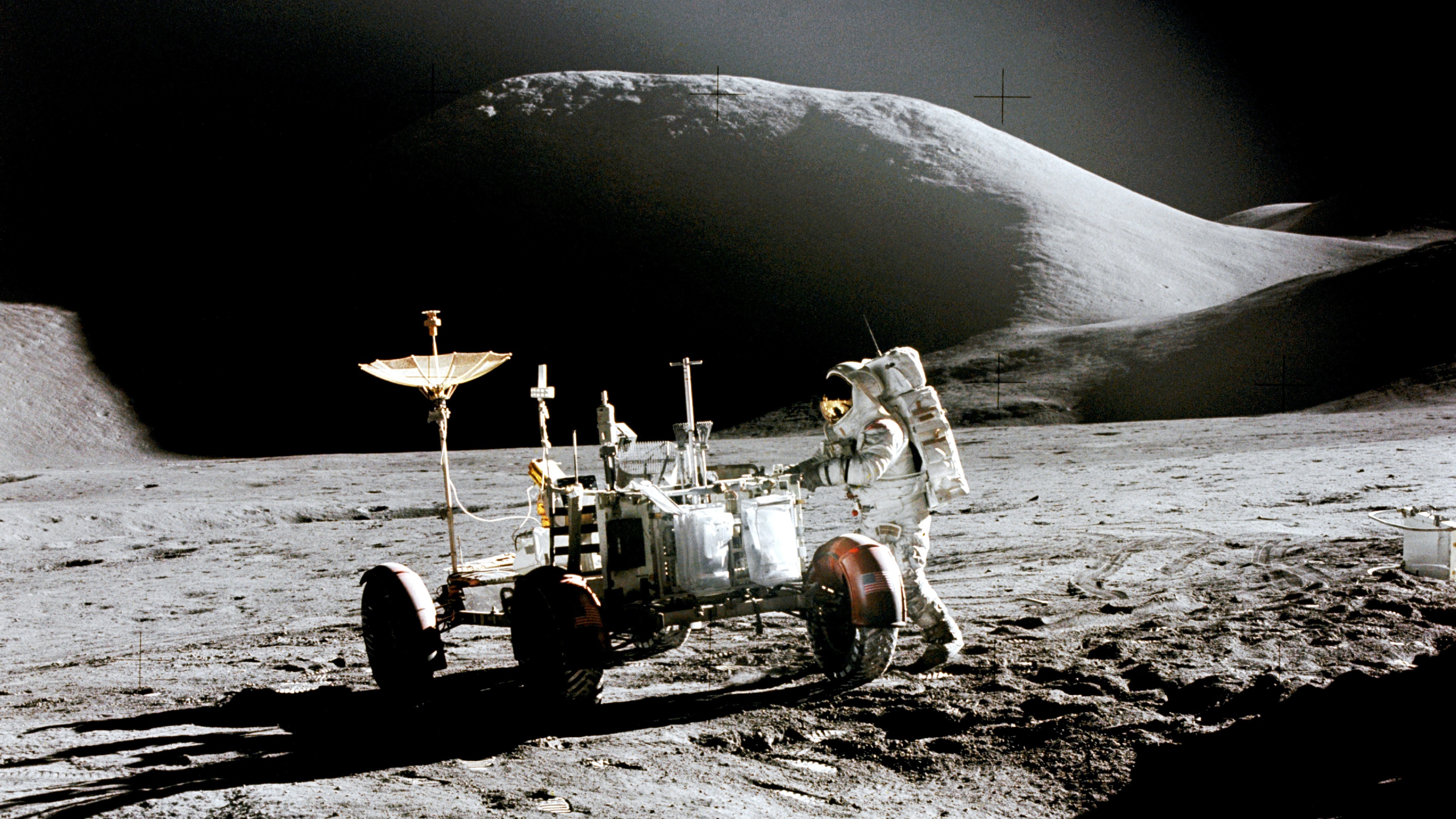 An astronaut standing next to a car-like vehicle on the moon.