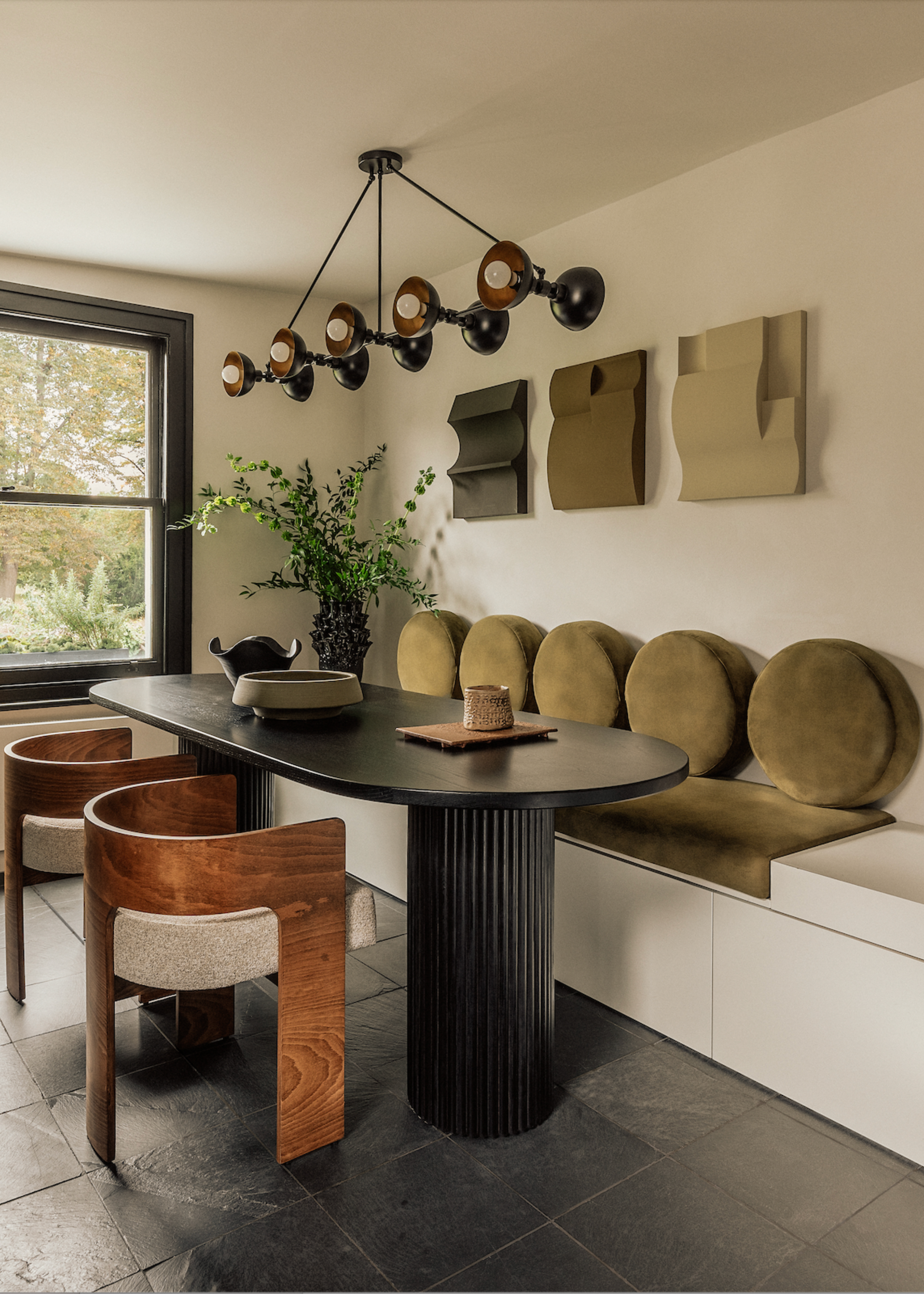 A living room with a black table, wood chairs and an upholstered bench with circular pillows