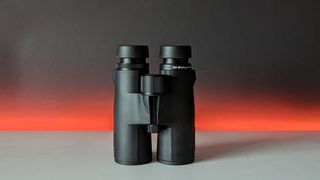 Svbony SV47 10x42 binoculars on a white table with a red light behind