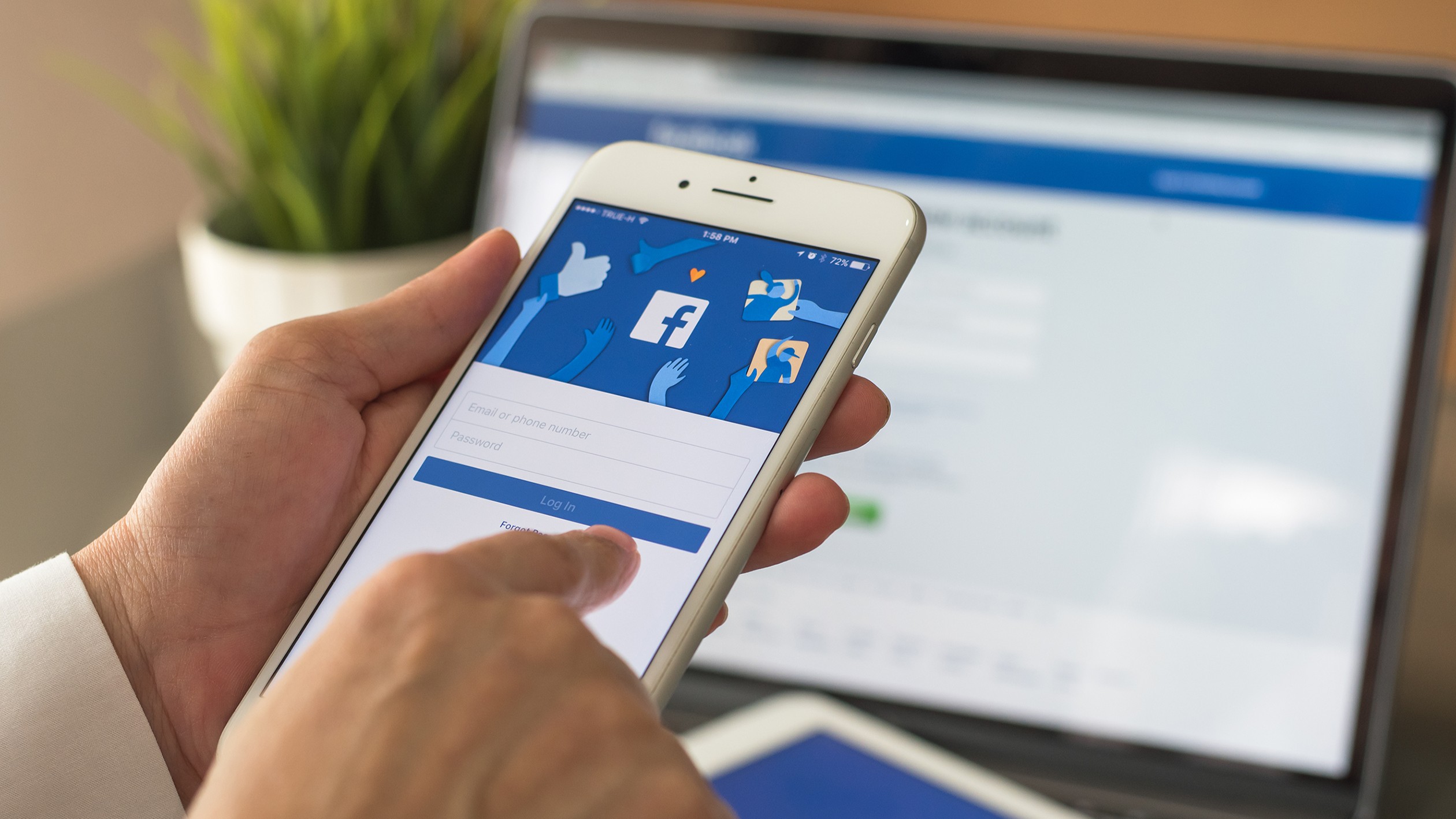 A person logging into Facebook on their phone with the site also open on a laptop in the background