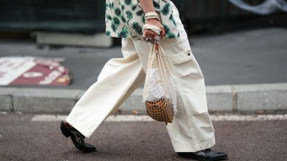 guest wears a beige with green leaves print pattern short sleeves shirt, a black shiny leather nailed / studded belt, pale yellow large cargo pants, a white latte mesh cotton handbag, black shiny leather with white embroidered seams shoes, silver rings , outside JW Anderson, during the Milan Fashion Week - Menswear Spring/Summer 2024 on June 18, 2023 in Milan, Italy. (Photo by Edward Berthelot/Getty Images)