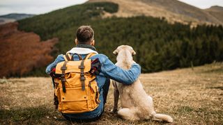 Man with arm around dog looking across at hills