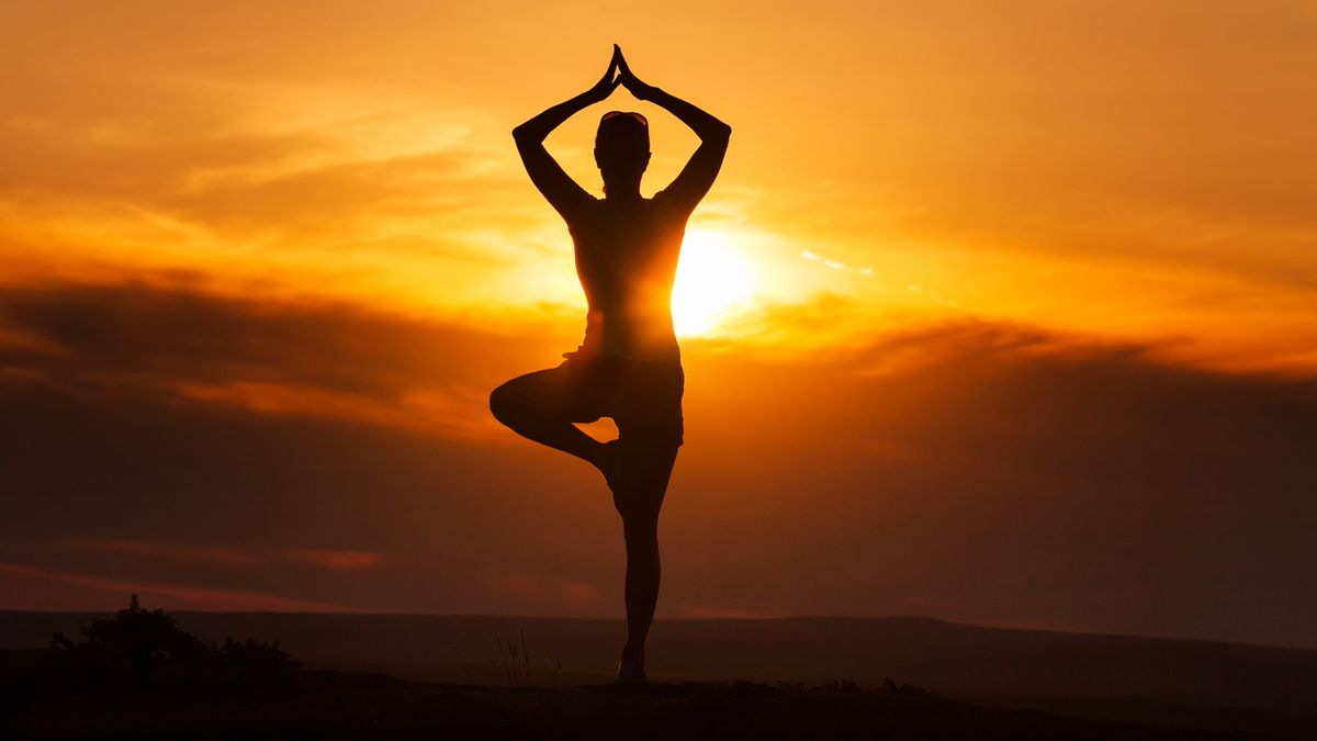 Is yoga a religion? image shows woman doing tree pose before a sunset