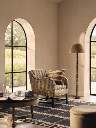 An armchair in the corner of a bright living room with large arched windows and a large area rug