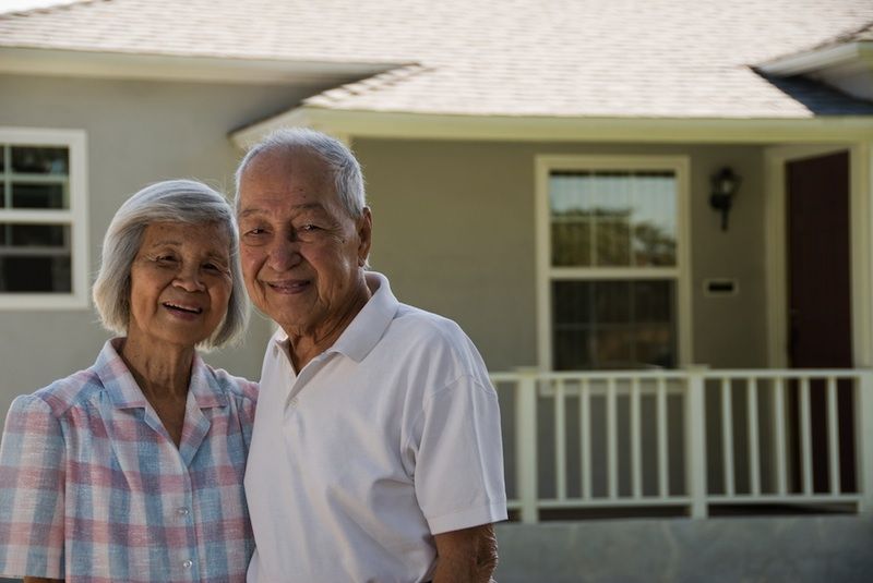 Elderly asian couple in front of their home.