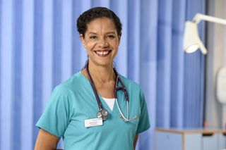 A smiling Jaye Griffiths as doctor Elle Gardner in Casualty wearing bright blue scrubs.