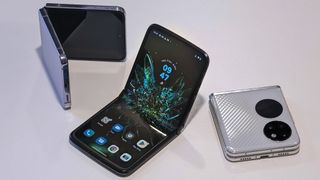 Motorola Razr 2022, Huawei P50 Pocket ja Samsung Galaxy Z Flip 4 arranged valkoisella pöydällä