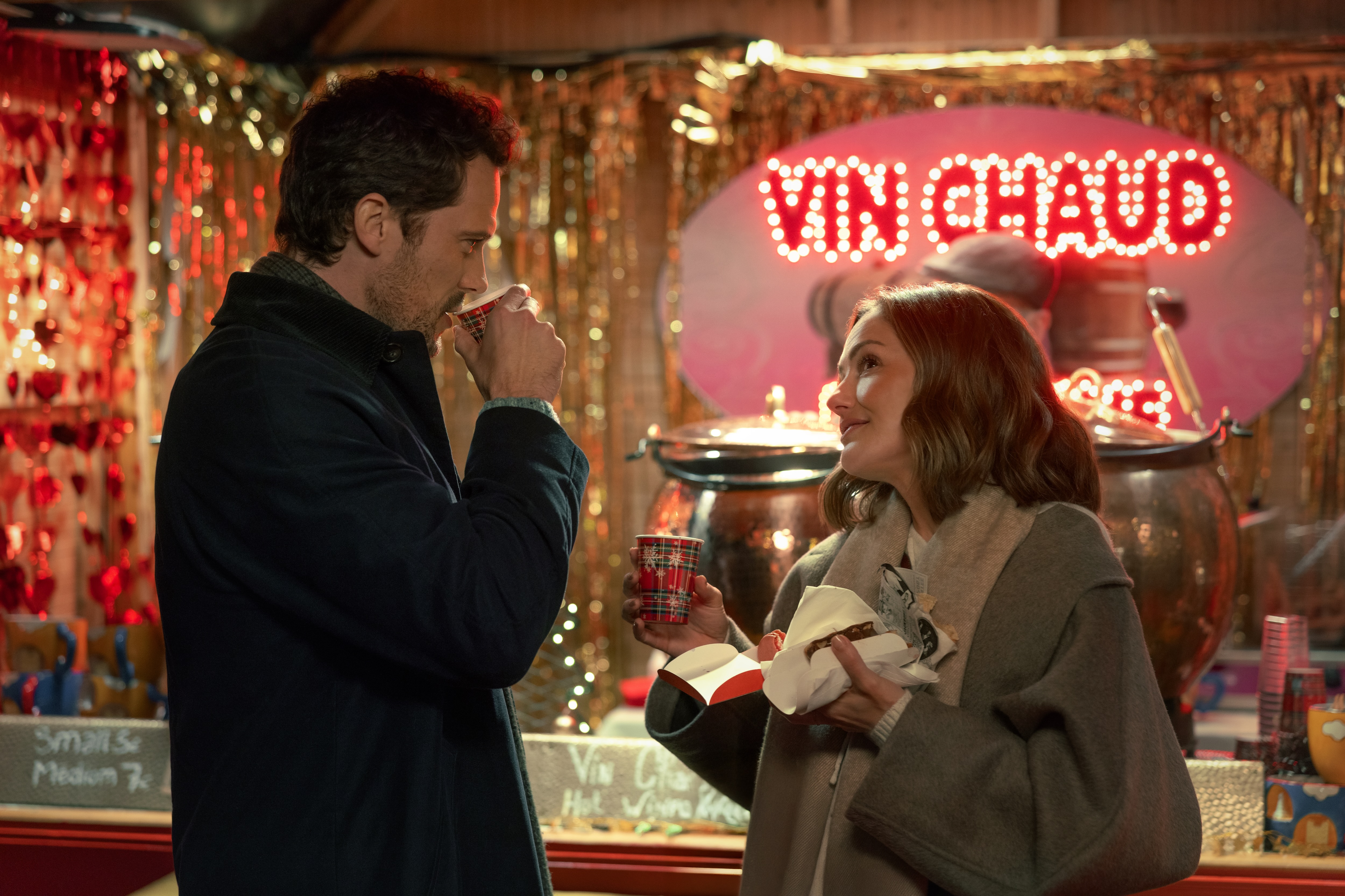 Champagne Problems. (L-R) Tom Wozniczka as Henri Cassell and Minka Kelly as Sydney Price as they drink hot cocoa outside of a holiday window display in Champagne Problems. Cr. Mika Cotellon/Netflix &amp;copy; 2025.
