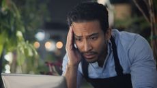 A restaurant owner looks stressed as he gazes at his laptop.