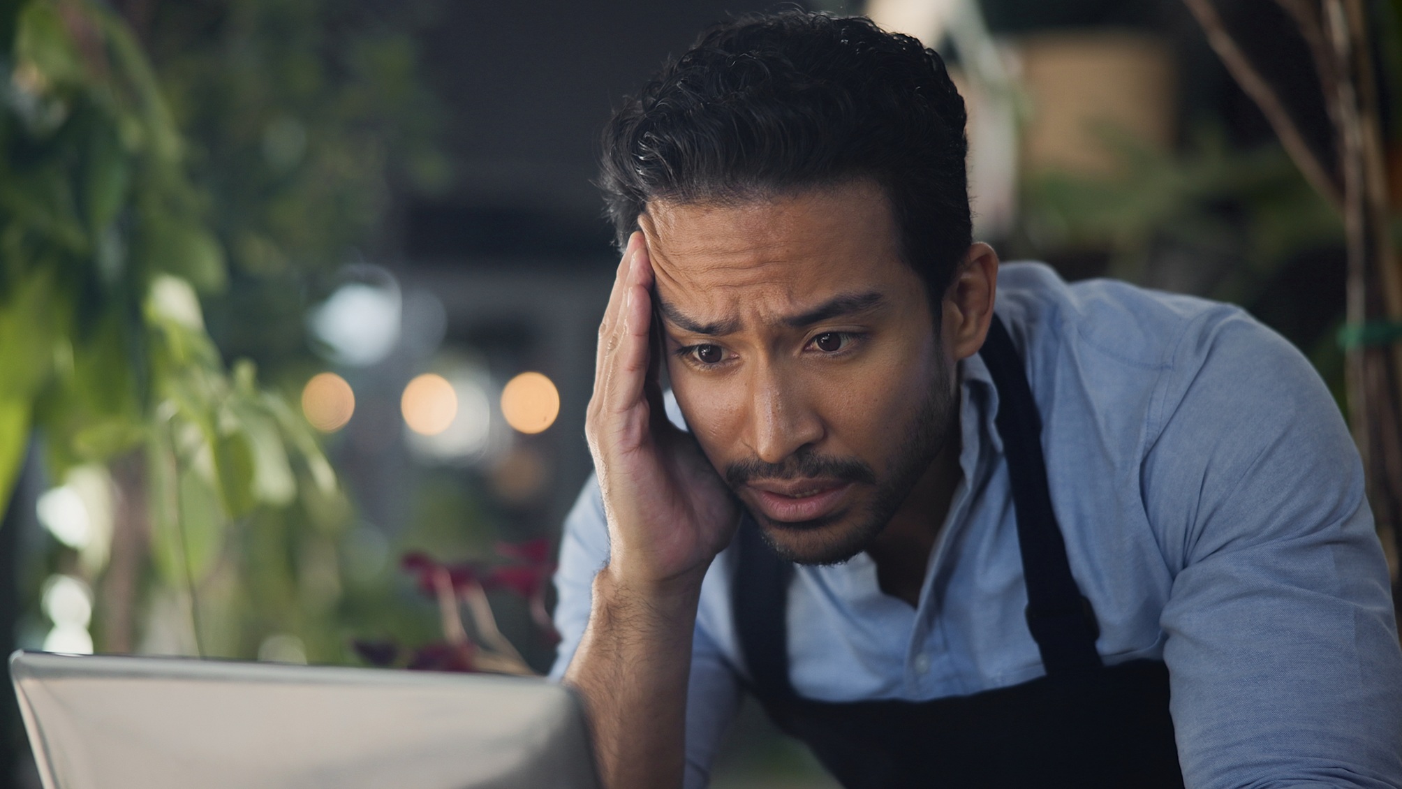 A restaurant owner looks stressed as he gazes at his laptop.