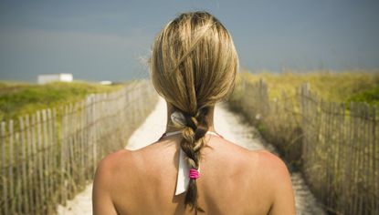 blonde woman at the beach with head turned to us showing a ponytail braid