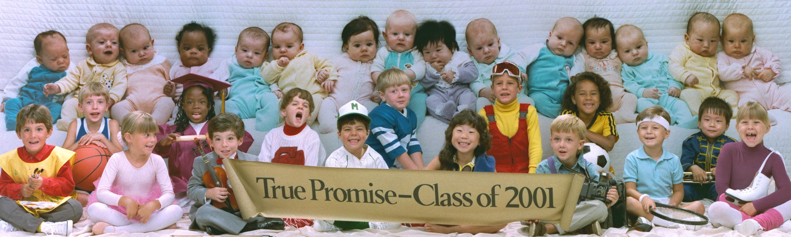 A row of babies in pastel sleepsuits sits on a quilted backdrop above a row of laughing children dressed as a painter, ballerina, violinist, baseball player, skier, tennis player and more, holding a banner reading &amp;ldquo;True Promise &amp;ndash; Class of 2001&amp;rdquo;.