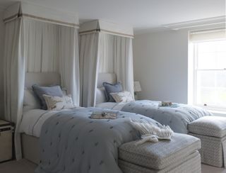 Twin beds with white canopies around a headboards and storage space at the ends of the beds showing hotel-style shared bedroom ideas.