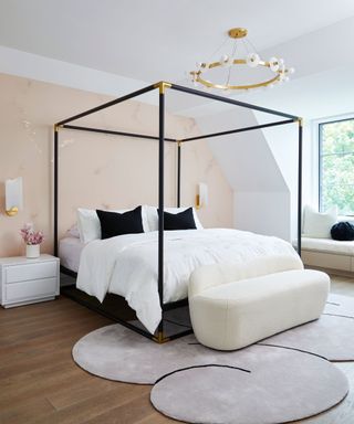 An Ali Budd modern four-poster with white sheets and black pillows against a pink accent wall