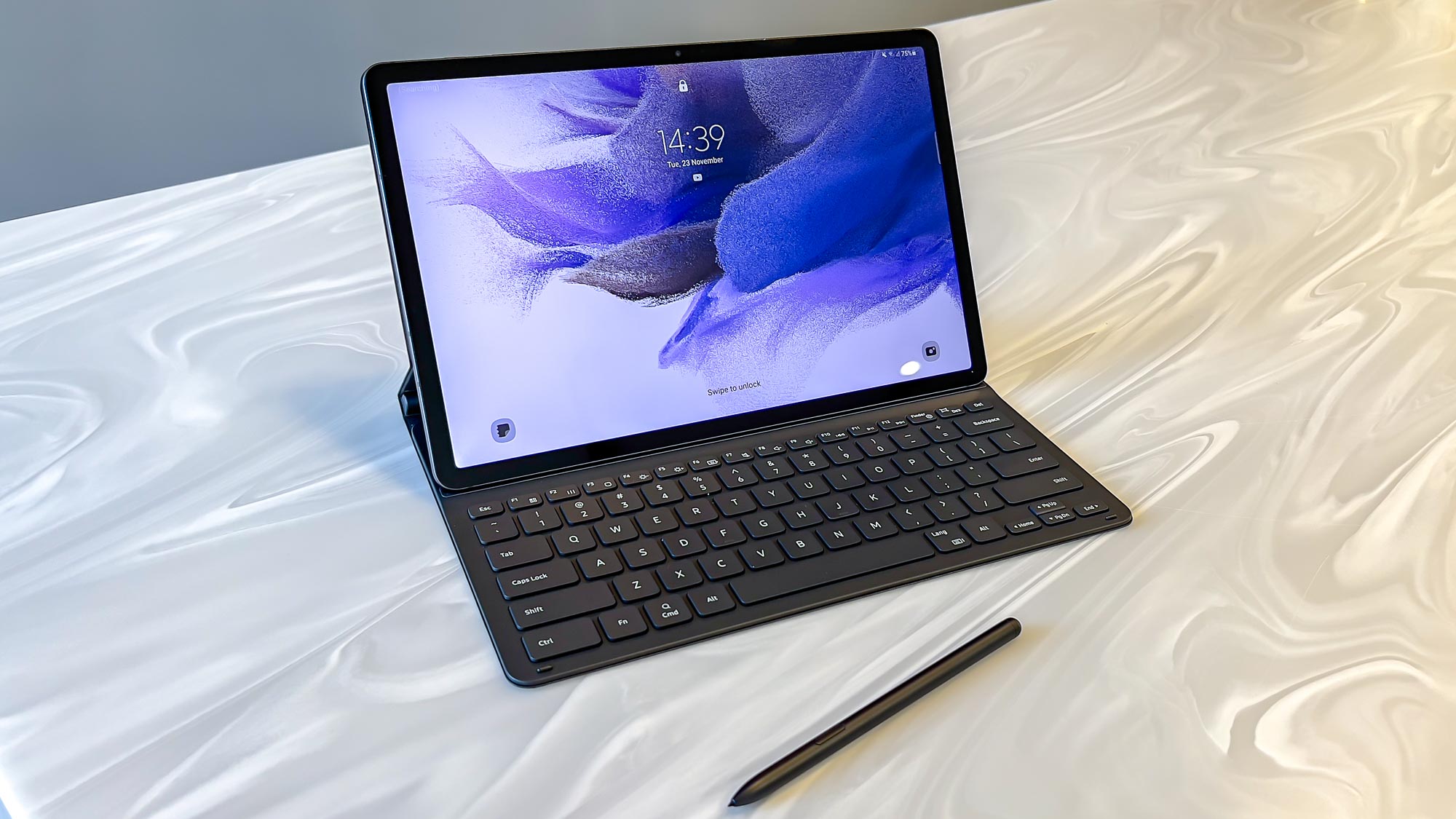 The Samsung Galaxy Tab S7 FE stood on a table with its keyboard case and an S Pen in front of it