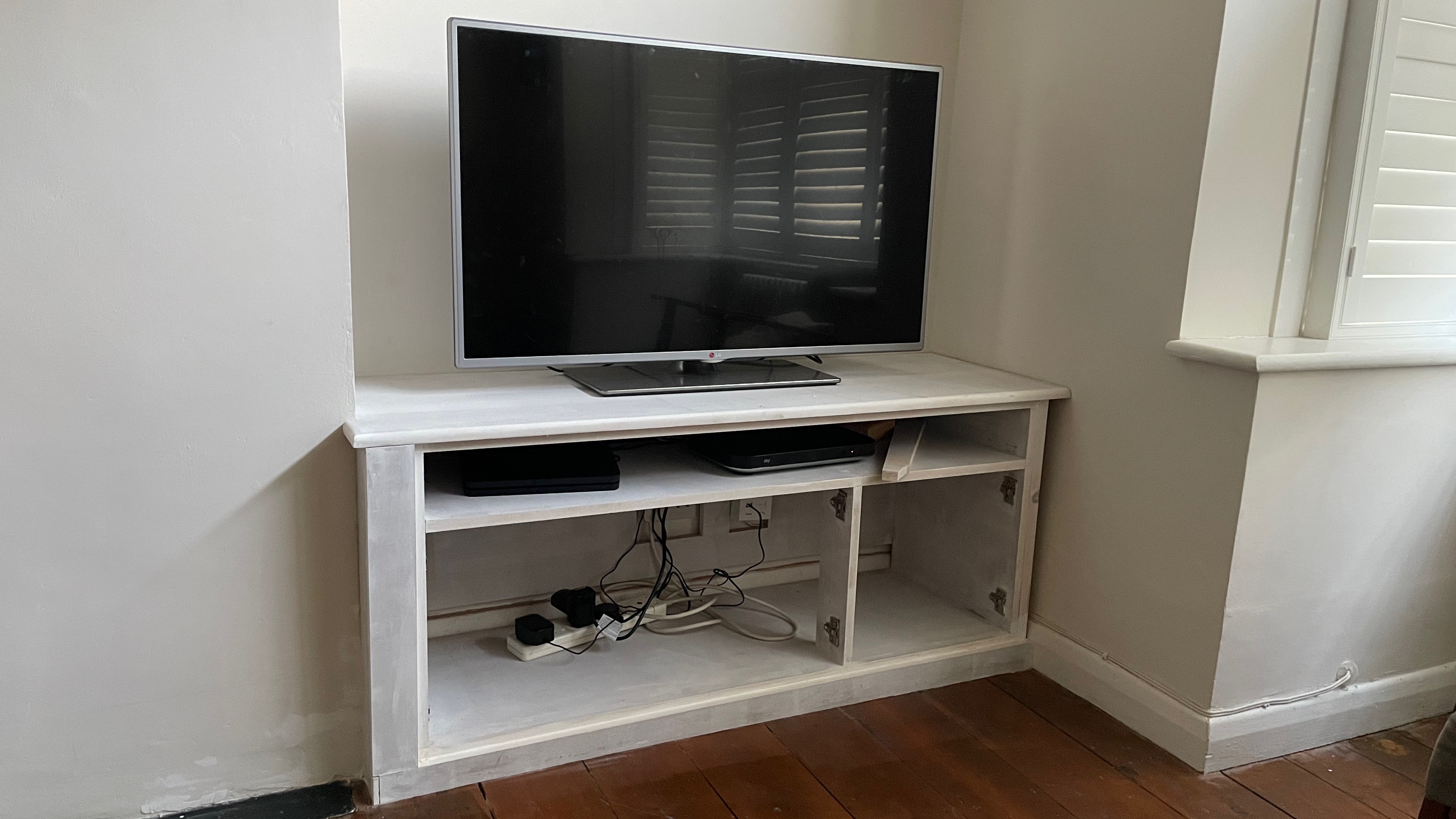 A TV cabinet in progress, unpainted, with no doors showing the cables running from the TV to the plug sockets.