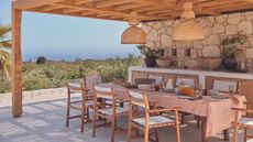 An outdoor terrace with a pergola and wooden / canvas chairs around a dining table