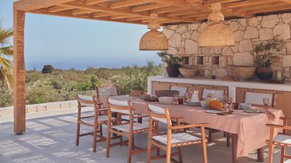 An outdoor terrace with a pergola and wooden / canvas chairs around a dining table