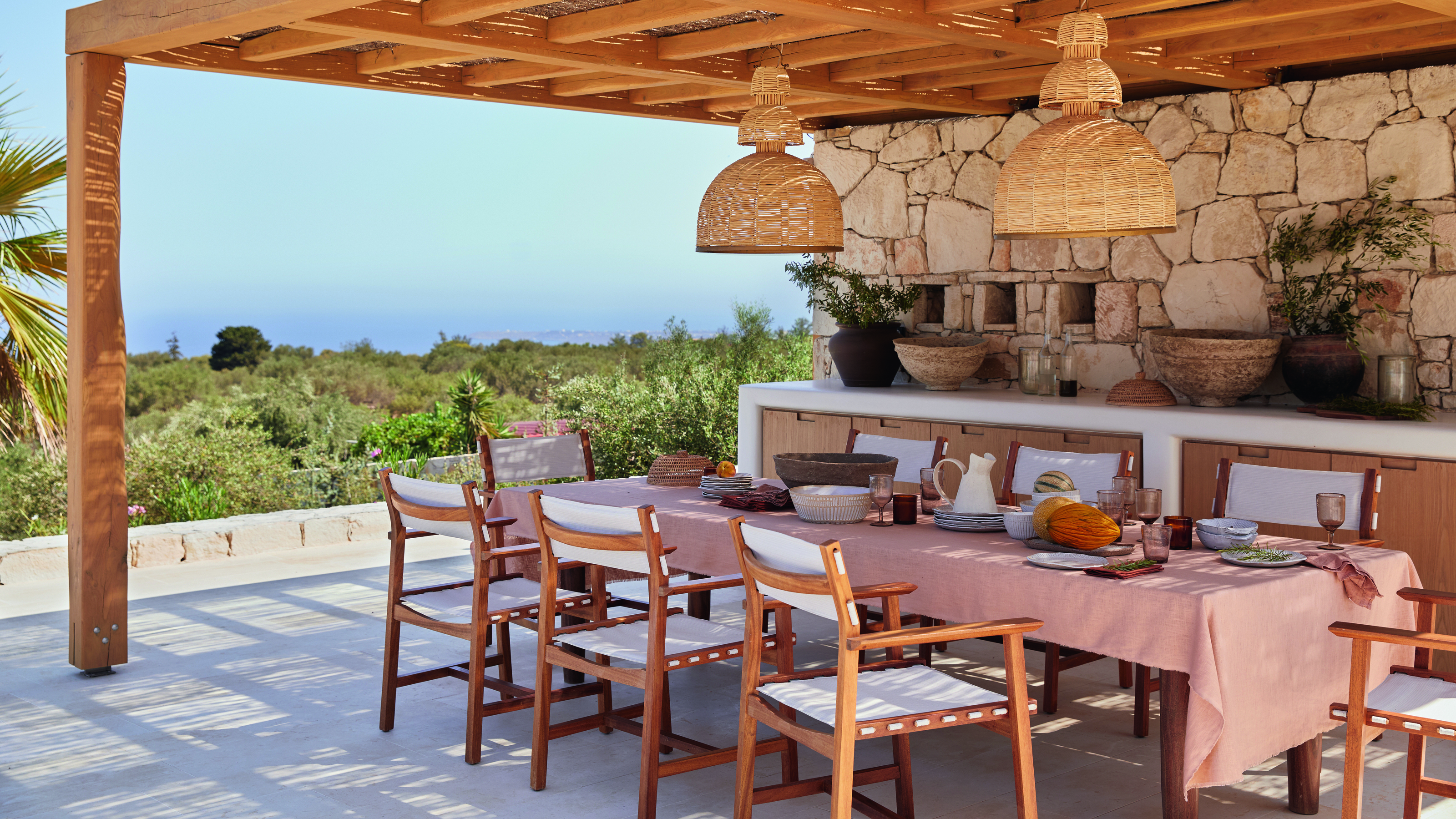 An outdoor terrace with a pergola and wooden / canvas chairs around a dining table