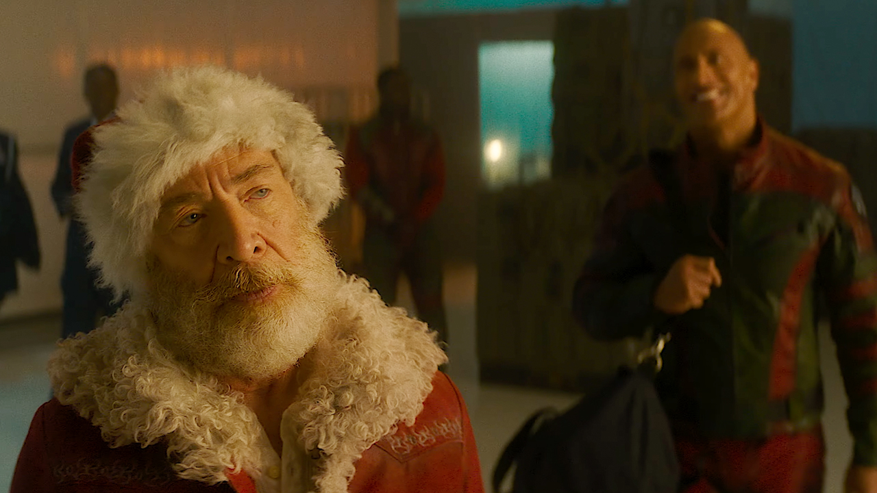 J.K Simmons looking a little annoyed but suited up to go, as Santa, while Dwayne The Rock Johsnon lingers in the background looking happy as a clam, in Red One. 