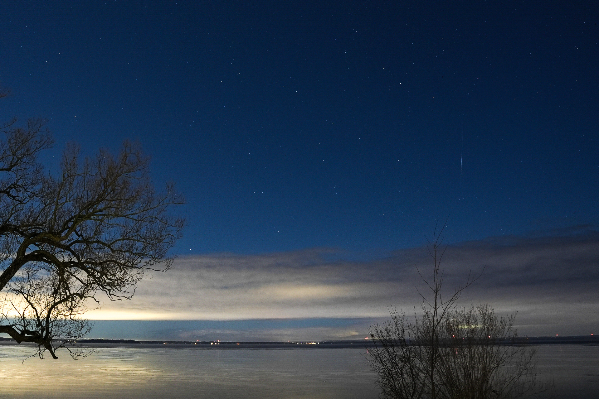  A meteor streaks across the night sky over Lake Simcoe, low cloud blocks the bright moonlight and a tree is in the foreground