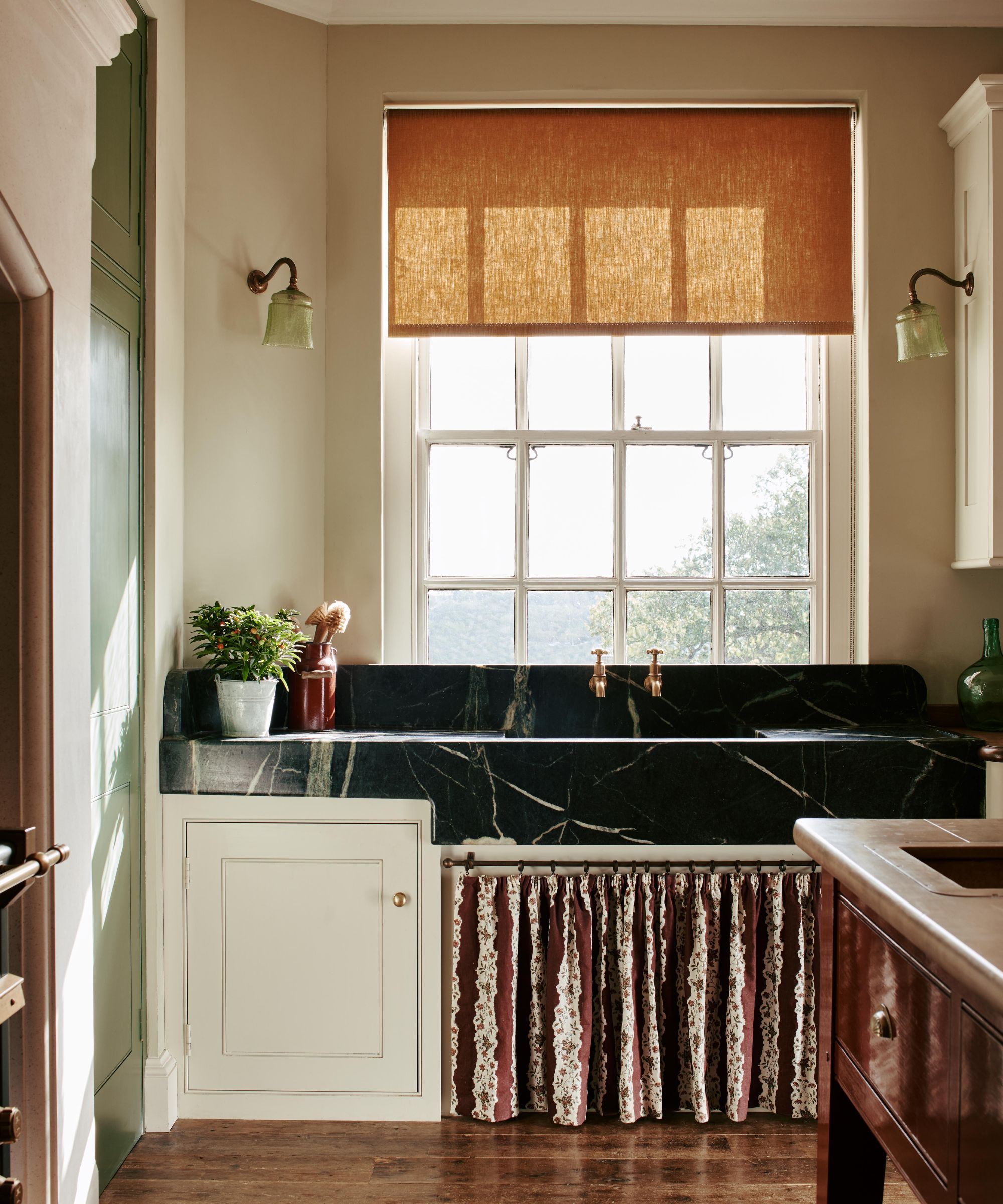 A traditional kitchen with a large black stone sink beneath the window with a floral sink skirt below