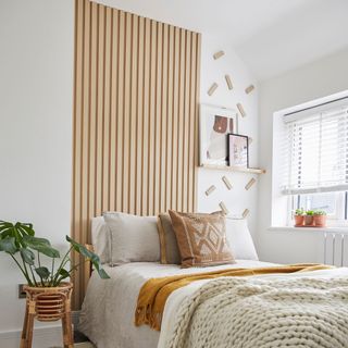 White bedroom with vertical blonde wood panelling behind bned