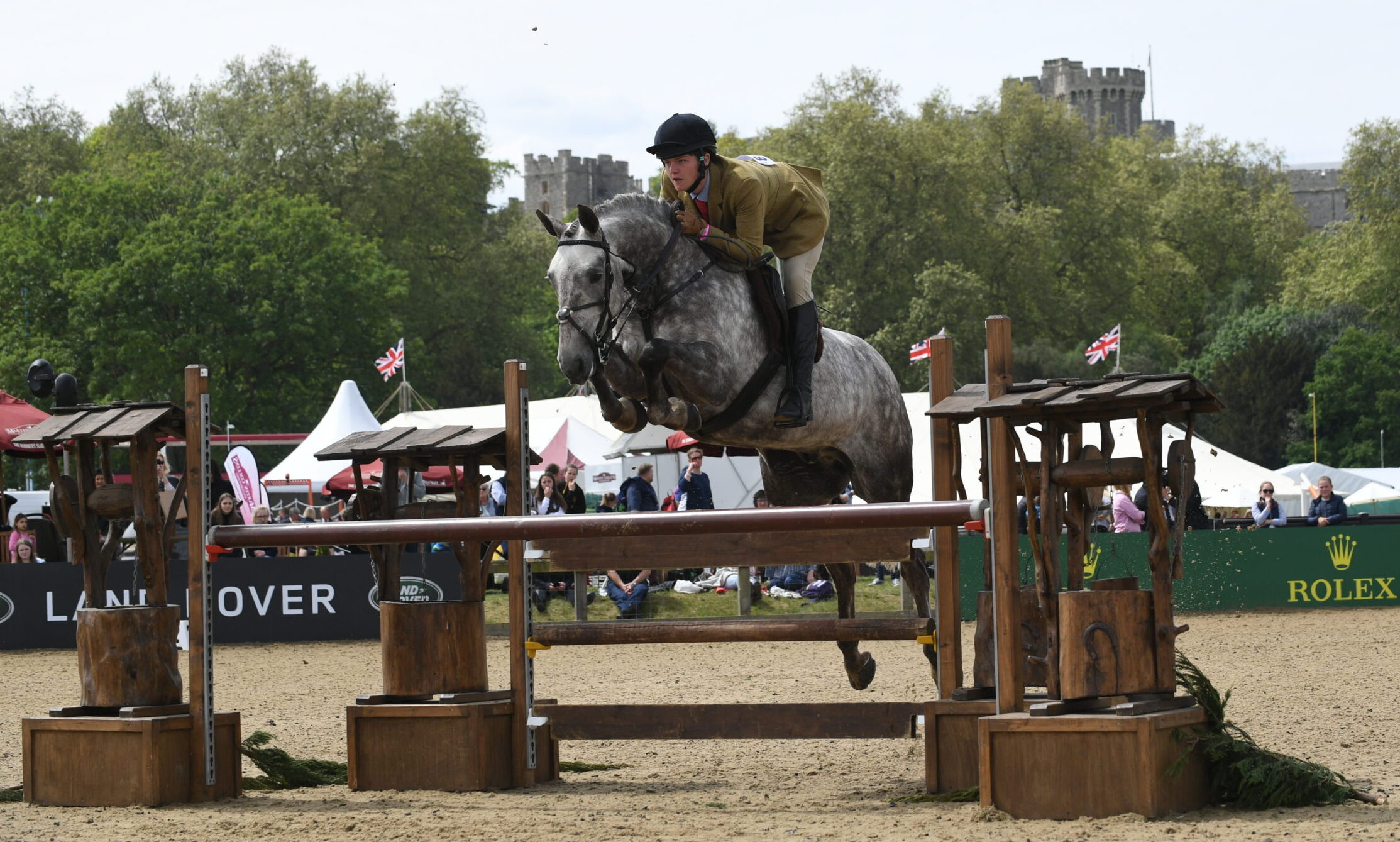A grey pony jumps a rustic fence in the working hunter pony section at Royal Windsor.