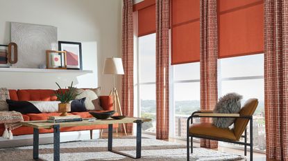 Colorful living room with large red curtains and blinds, red sofa, wooden coofee table and armchair, white rug, and misc art on a floating white shelf.