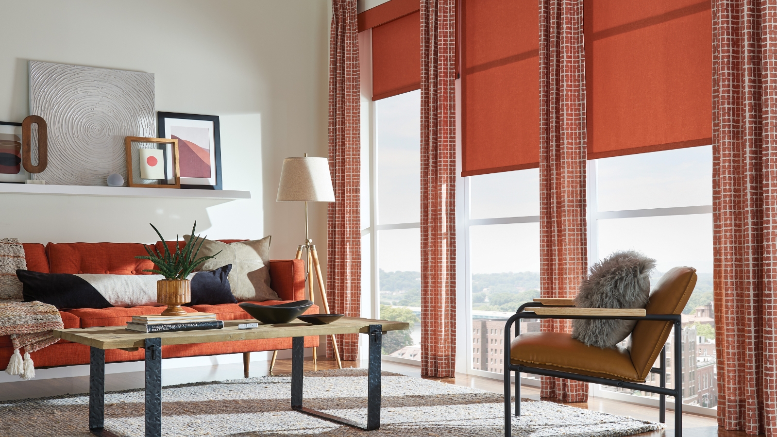 Colorful living room with large red curtains and blinds, red sofa, wooden coofee table and armchair, white rug, and misc art on a floating white shelf.