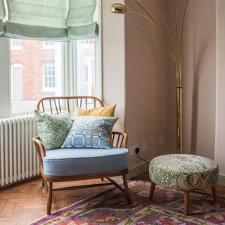 pink living room with an ercol mid-century-style armchair in a bay window with upholstered footstool