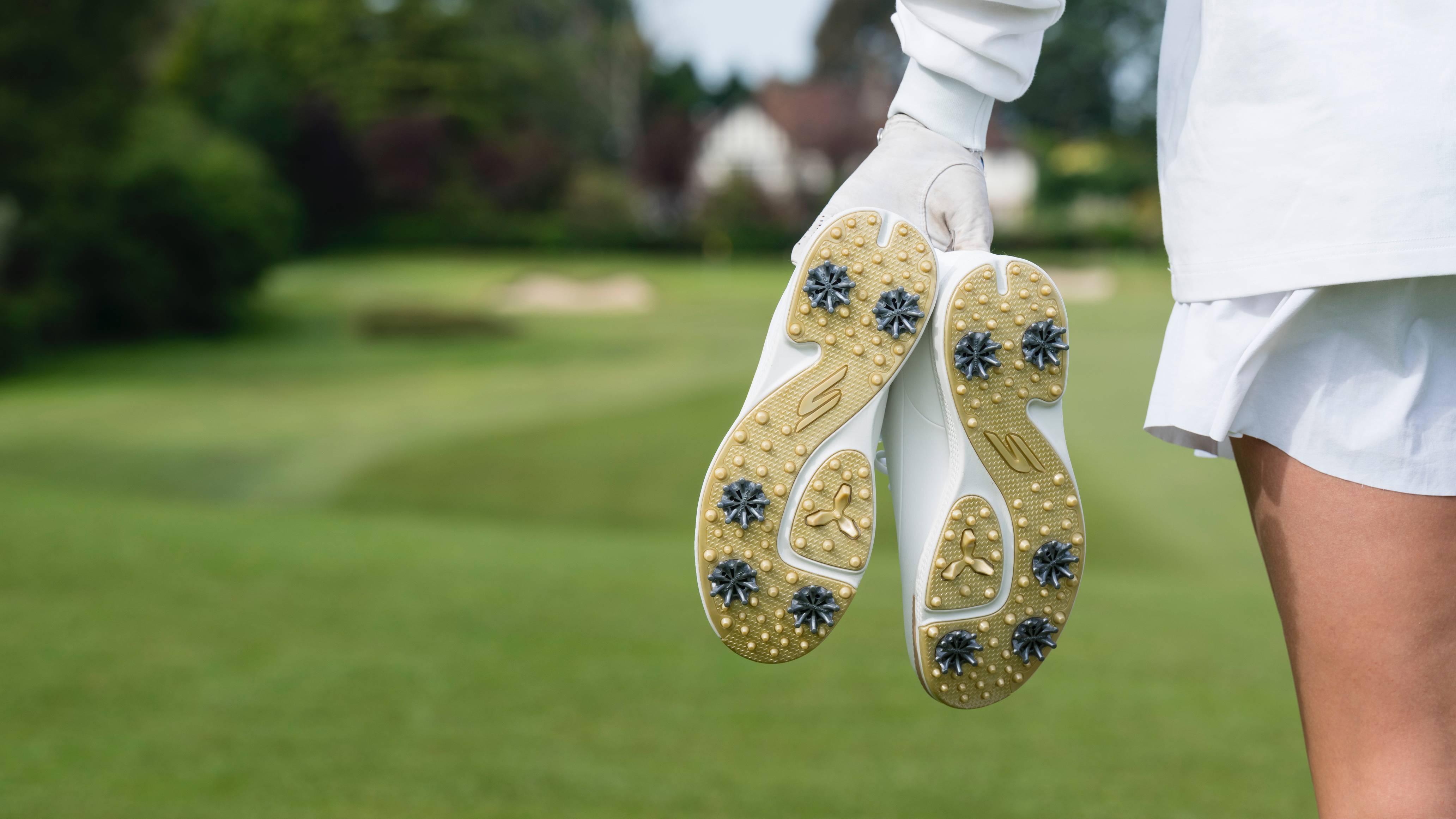 Female golfer holding a pair of spiked golf shoes