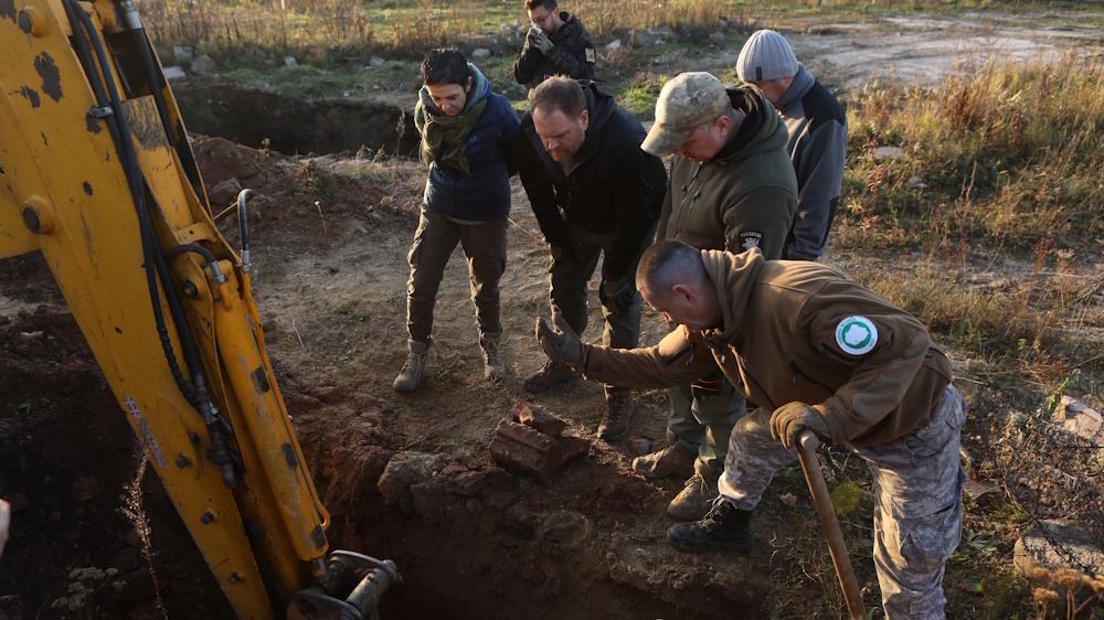 Host Josh Gates, Joanna Lamparska, Krzysztof Mężyk and team watch an excavator dig near a tunnel in Poland as they search for evidence of the Amerikabomber.