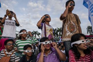 Skywatchers observe the sun with solar-viewing glasses and card viewers.