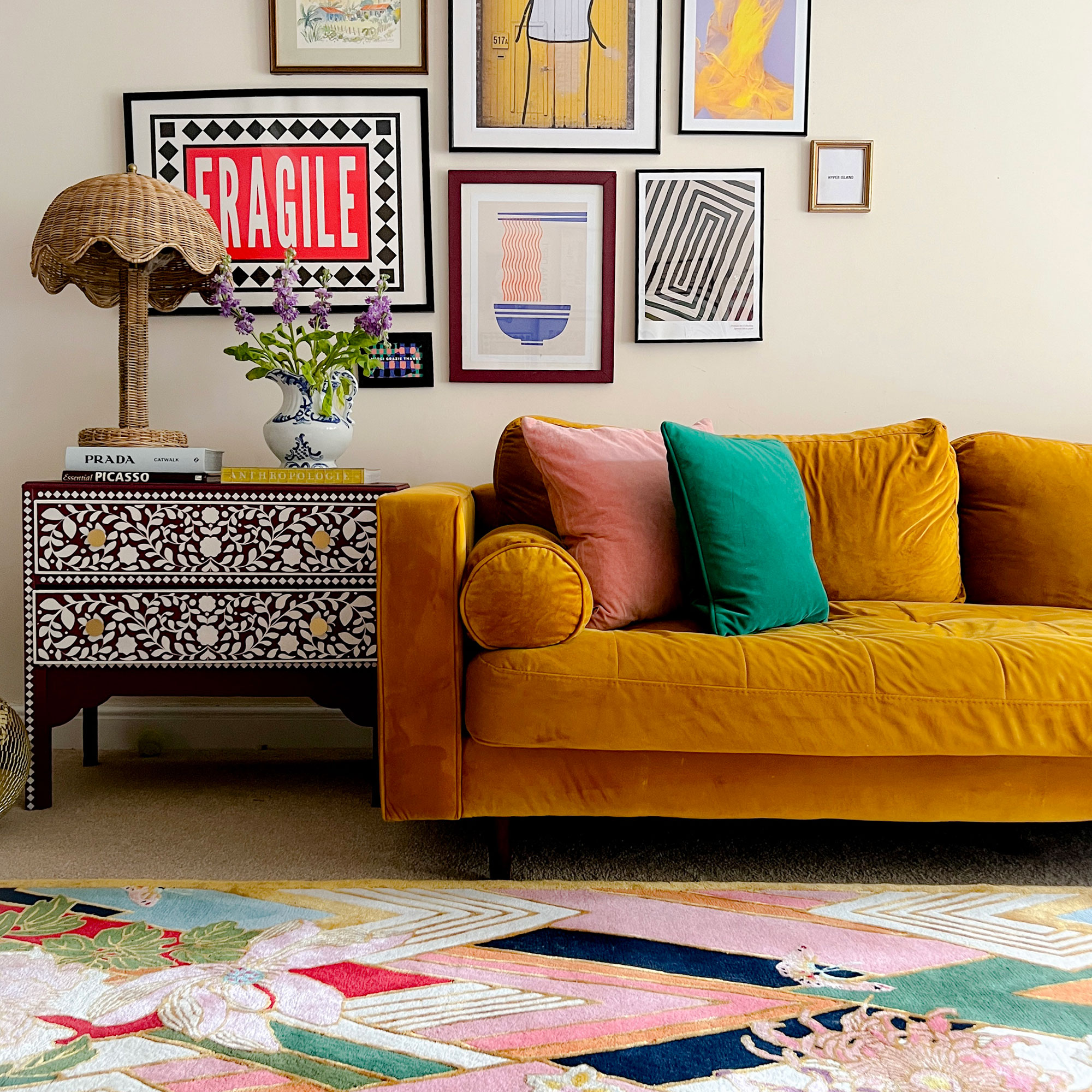 Colourful patterned rug in front of gold sofa and inlaid side table with drawers 