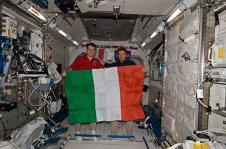 Inside the International Space Station (ISS), European Space Agency astronauts Paolo Nespoli (left) and Roberto Vittori unfurl the Italian flag during an Earth-to-space phone tag-up with Italian President Giorgio Napolitano. The conversation took place on