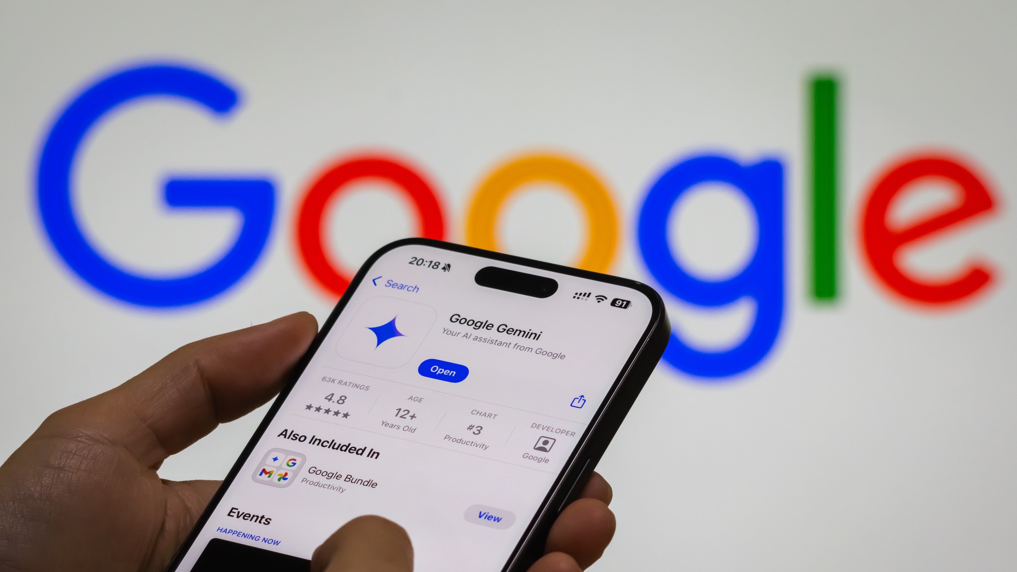 A person interacts with the “Google Gemini” app on a smartphone, with the Google logo in the background.