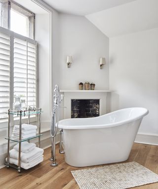 A white bathroom with a standalone tub, towel stand and ornamental fireplace