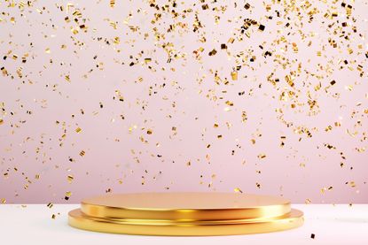 Two-tier round gold metal podium on pastel pink background with many falling gold confetti